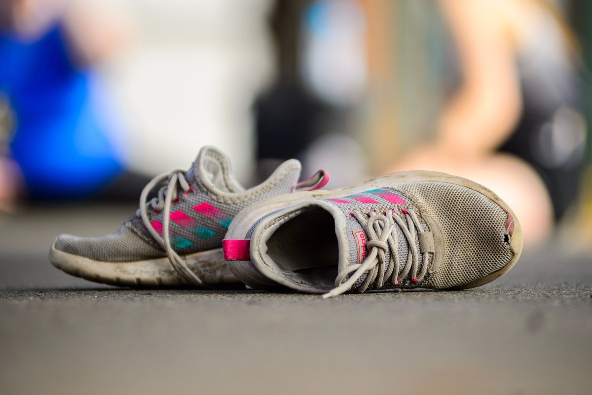 A worn pair of running shoes lying on tarmac, soles scuffed and uppers dirty