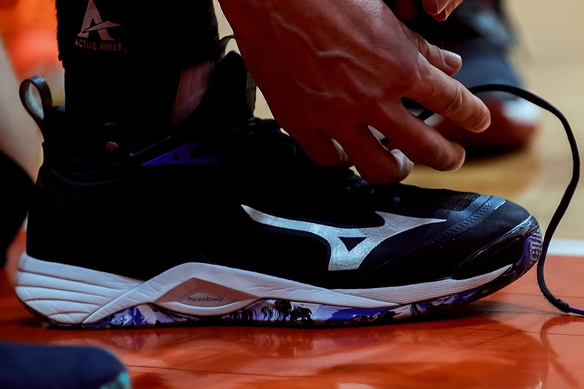 A hand lacing a Mizuno court shoe on a wooden floor, the midsole in full view